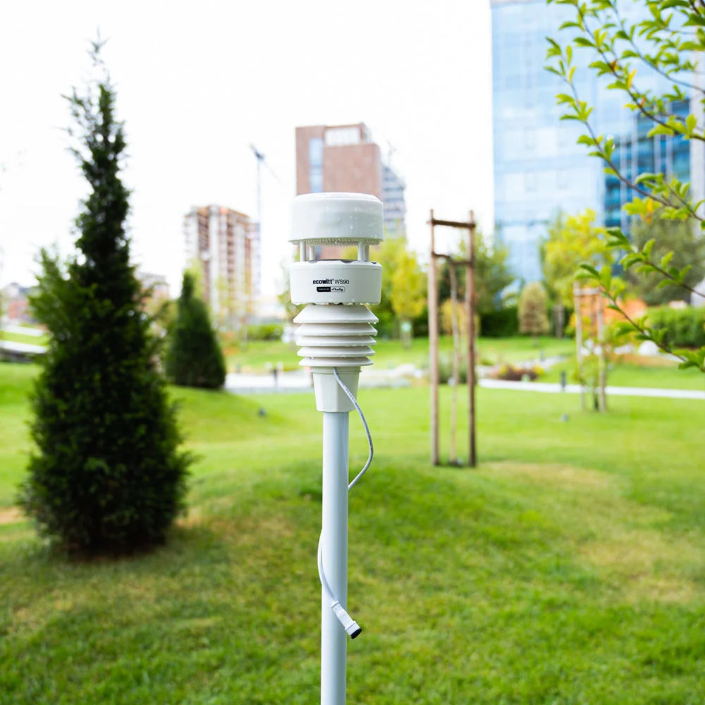 White Ecowitt weather station on a pole in a park with buildings in the background | Lykalyte