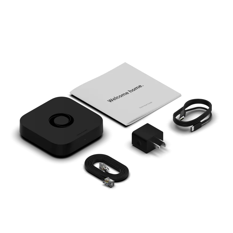 Homey Pro Mini kit on a clean white background, including a black square control receiver, a white welcome booklet, a black power adapter, a black cable with a connector, and a black wristband. | Lykalyte