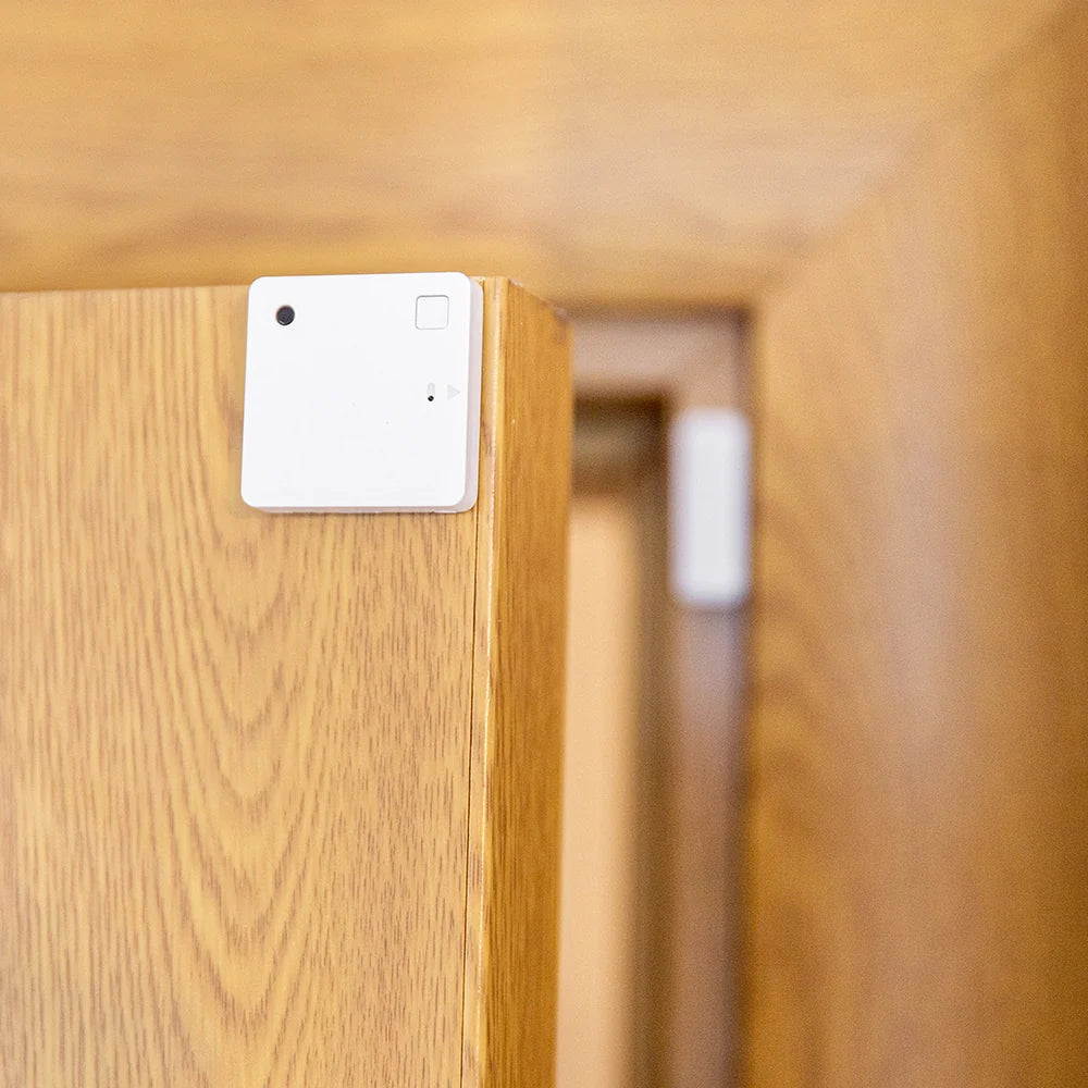 Small Square White Shelly device on top corner of wooden door with small with rectangle magnet in background on door frame | Lykalyte